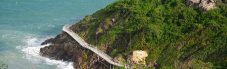 Panorama aerial view timber boardwalk built over rocks mountain side by the ocean with tourist walking, elevated walkway viaduct for pedestrians in remote vacation island in Nha Trang, Vietnam. Travel