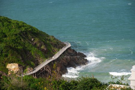 Aerial view timber boardwalk built over rocks mountain side by the ocean with tourist walking, elevated footpath walkway viaduct for pedestrians in remote vacation island in Nha Trang, Vietnam. Travel