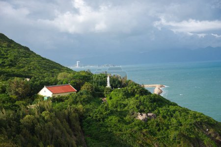 Vietnamese Buddhist temple and Guanyin statue at mountain top with downtown Nha Trang background, lush green tropical forest by the ocean blue waves turquoise water, aerial coastal embankment. Vietnam