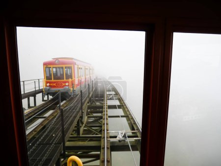 Heritage tram train on lifted aerial electric light rail transit covered in foggy misty winter weather, scenic mountain landscape, railway from Sapa to Muong Hoa Station cable car Fansipan. Vietnam