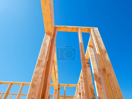 Wooden exterior and interior walls framing house with rough openings for doors and windows on newly set foundation of medium size single family residential home in Dallas, Texas, clear blue sky. USA
