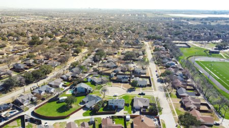 Aerial view upscale residential neighborhood with downtown skyline in distance background, single family houses with large backyard, swimming pool, wooden fence near school football field, Dallas. USA