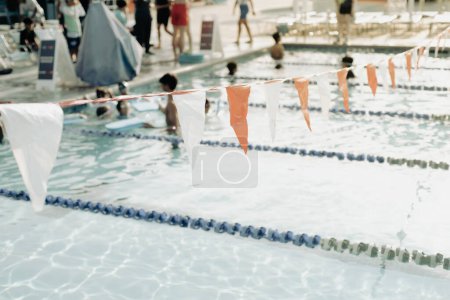 Toned photo backstroke flags and blurred swimming class little kids with coach and parents audience at public competitive swimming pool summertime, Dallas, Texas, pool lane divider rope floats. USA