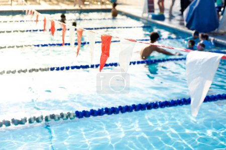 Banderas de espalda y clase de natación borrosa para niños pequeños con audiencia de entrenadores y padres en la piscina competitiva pública de verano en Dallas, Texas, cuerda divisoria de carril de piscina y carrozas. Estados Unidos