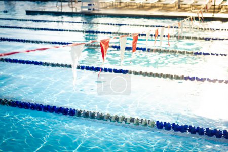 Cadena DOF poco profunda de banderas triangulares coloridas de espalda que cuelgan sobre la piscina pública competitiva con cuerda divisoria de carril de piscina y flotadores, agua limpia sin nadador, Dallas, Texas, saludable. Estados Unidos
