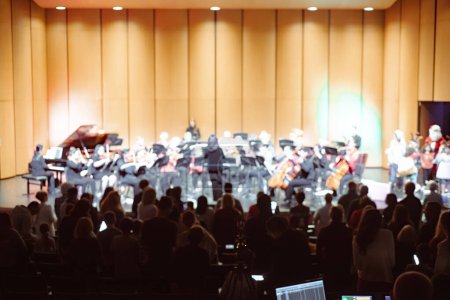 Photo for Motion blurred symphony orchestra, children choir, holiday themed diverse performers, conductor, audience stood up to cheer, wind, bass, percussion instruments, violin, cello, trumpet, piano, TX. USA - Royalty Free Image