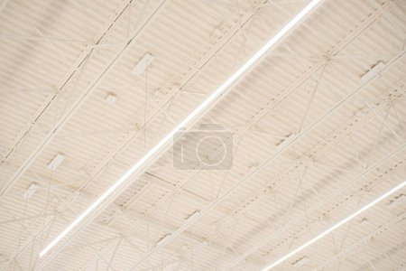 Long shop LED lights hanging over modern suspended ceiling metal roof structure, warehouse industry factory building lighting solution background, perimeter track membrane truss, Frisco, TX. USA