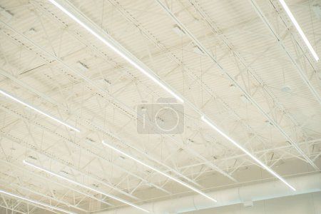 Long shop LED lights hanging over modern suspended ceiling metal roof structure, warehouse industry factory building lighting solution background, perimeter track membrane truss, Frisco, TX. USA