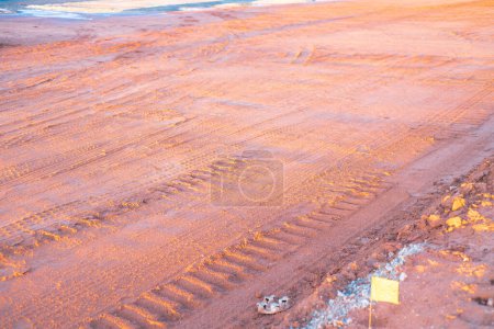 Yellow marking flag and groundworks with heavy truck tire tread traces, gravel pile at construction site during sunset, prepare ground foundations, high quality industrial background, Oklahoma. USA