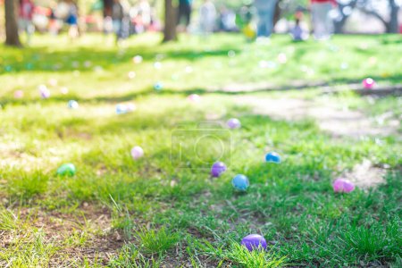 Téléchargez les photos : Abondant d'œufs de Pâques colorés sur un champ d'herbe verte avec des gens flous divers enfants parents attendent derrière la barricade de ruban vinyle pour la chasse aux œufs tradition de collecte à l'église locale, Dallas, TX. États-Unis - en image libre de droit