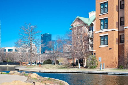 Hotels, buildings along Bricktown canal with downtown Oklahoma City skyline background, riverside restaurants, tourist attractions in Entertainment District, travel destination, water taxi. USA