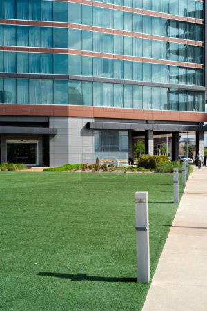 Concrete pathway with solar lights to entrance of multistory urban modern hotel glass wall blackout curtains in downtown Irving, Texas, large artificial grass courtyard, exterior building. USA