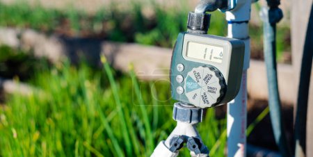 Photo for Panorama large display of water timer at community garden in Dallas, Texas, outlet hose faucet digital timer with Y splitter connector automate drip irrigation system, water energy conservation. USA - Royalty Free Image