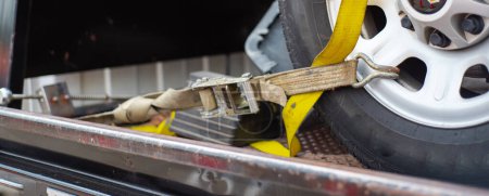 Panorama smashed bumper front fender on pickup truck by car accident on flatbed rollback tilt tray of tow truck with yellow ratchet strap tie down, collision, insurance claim concept, Texas. USA