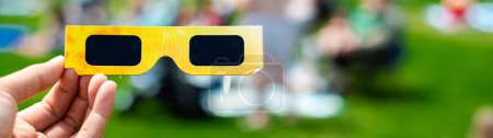 Panorama paper optics solar eclipse glasses scratch resistant polymer lenses filter harmful ultraviolet, infrared ray, blurry crow people on grassy yard watching totality show in Dallas, Texas. USA