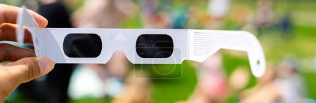 Panorama view paper optics solar eclipse glasses scratch resistant polymer lenses filter harmful ultraviolet, infrared ray, blurry crow people on grassy yard watching totality show, Dallas, Texas. USA