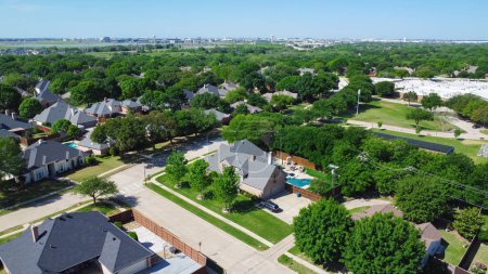 Suburban residential neighborhood with downtown Dallas, Texas in distance background, large upscale two-story single-family house, swimming pool, wooden fence backyard, lush green tree, aerial. USA