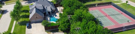 Panorama community tennis courts with chain link fence and players in upscale residential neighborhood, large two-story single-family house, swimming pool, large backyard, suburb Dallas, aerial. USA