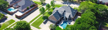 Panorama two story suburban single-family home with swimming pool, large backyard, tall wooden fence, suburb Dallas, TX subdivision, upscale house lush green tree, well-trimmed landscape, aerial. USA