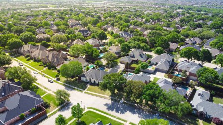 Aerial view lush greenery suburban residential neighborhood subdivision, row of upscale two-story houses with swimming pool, shingle roofing, large fenced backyard, well-trimmed HOA landscape. USA