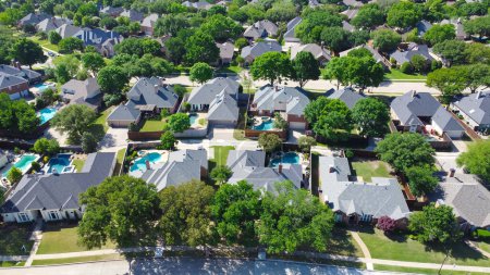 Aerial view lush greenery suburban residential neighborhood subdivision, row of upscale two-story houses with swimming pool, shingle roofing, large fenced backyard, well-trimmed HOA landscape. USA