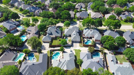 Shingle roofing of large two story suburban upscale houses lush greenery tree, swimming pool, large fenced backyard, well maintained HOA landscape in subdivision suburb Dallas, Texas, aerial view. USA