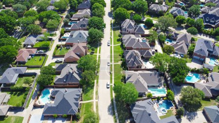Tree lined residential street with well-trimmed front yard of upscale two-story suburban houses with swimming pool, large fenced backyard, well-trimmed HOA landscape, Dallas, Texas, aerial view. USA