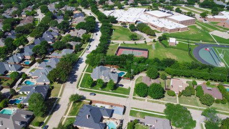 Upscale suburban neighborhood near school district, community tennis courts, football fields, residential houses with swimming pool, large backyard, tall matured tree, suburbs Dallas, aerial view. USA