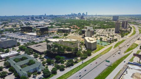 Grupo de edificios de oficinas, hoteles, restaurantes en el barrio Love Field con el centro de Dallas en el fondo, cielo azul claro soleado, tráfico ocupado en la autopista Stemmons I35, vista aérea. Estados Unidos