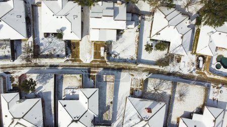 Straight aerial 90 degrees view of heavy snow cover shingles roofing, residential street suburban houses in Dallas-Fort Worth metropolitan area, severe weather, climate change, sunshine melting. USA