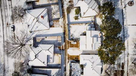 Straight aerial 90 degrees view of heavy snow cover shingles roofing, residential street suburban houses in Dallas-Fort Worth metropolitan area, severe weather, climate change, sunshine melting. USA