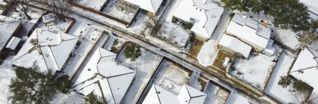Panorama view row of single-family houses covered in heavy snow on shingles roofing, residential street suburban Dallas-Fort Worth metropolitan, severe weather, climate change, sunshine melting. USA