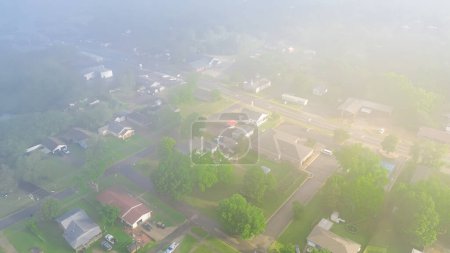 Foggy and misty morning light cover row of suburban houses near Gentry Avenue outside historic downtown of Checotah city in McIntosh County, Oklahoma lush green trees, aerial view small town. USA