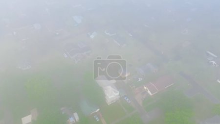 Heavy foggy over suburban houses near Gentry Avenue outside historic downtown of Checotah city in McIntosh County, Oklahoma lush green trees, aerial view small town, misty morning, early summer. USA