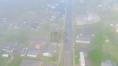 Foggy and misty morning light cover row of suburban houses near Gentry Avenue outside historic downtown of Checotah city in McIntosh County, Oklahoma lush green trees, aerial view small town. USA