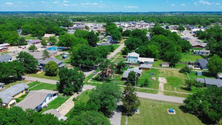 Checotah town of McIntosh County, Oklahoma with suburban residential houses, large backyard, historic downtown Broadway and Main Street background, lush green tree in horizontal line, aerial. USA