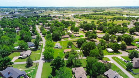 SW 4th street in Checotah, McIntosh County, Oklahoma with Interstate I-40 and water tower in background, row of single-family homes with large backyard, surrounding by lush green trees, aerial. USA