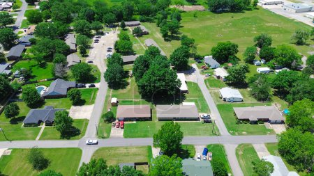 Neighborhood with cemetery in Checotah, McIntosh County, Oklahoma, row of single-family houses with large backyard lot size along SW 5th Street, grassy lawn, lush green tall mature trees, aerial. USA