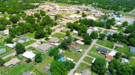 Aerial view residential suburbs houses in Checotah, McIntosh County, Oklahoma toward Broadway and Main Street with historic downtown buildings background, small town landscape, lush green trees. USA