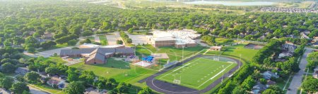 Panorama view lakeside urban sprawl green neighborhood, school district sport complex football field, tennis court, running track, playground in residential area Dallas Fort Worth suburbs, aerial. USA