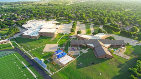 Middel and elementary school in upscale suburban residential area subdivision with football field and playgrounds, surrounding lush green trees North of Dallas Fort Worth Metro complex, aerial. USA