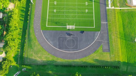 Football fields with yard lines 10-yard increments, running track, soccer goals, tire flip training at middle school grassy lawn artificial turf, suburbs Dallas Fort Worth Metro complex, aerial. USA