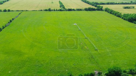 Center pivot irrigation on large farm grassland in Fairland, Oklahoma, stainless steel pipeline with mobile truss structures motorized wheels allowing pipe to move through the field, aerial view. USA