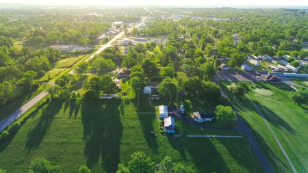 Service road with power line in countryside Mountain Grove Missouri thru lush greenery trees, meadows and farm houses with ponds in agricultural area, peaceful rural lots in Midwest, aerial view. USA