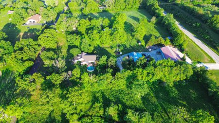 Lush greenery tree surrounding large farm houses with portable pop-up swimming pool near country road in Mountain Grove Missouri, farmland ranches in the Midwest, agricultural area, aerial view. USA