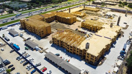 Apartment under construction near Interstate I-35E Stemmons Freeway downtown Dallas, timber wood frame, elevator vertical shaft, large courtyard, slab foundation, heavy equipment, aerial view. USA