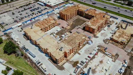Aerial view workers and heavy industrial machines working at apartment complex construction, timber wood frame, elevator vertical shaft, large courtyard, slab foundation in downtown Dallas, Texas. USA