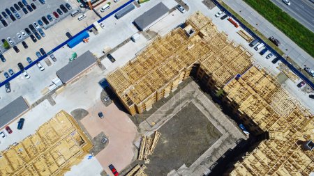 Multistory apartment complex under construction with timber wood frame, elevator vertical shaft, large courtyard, slab foundation, heavy equipment machines, downtown Dallas, Texas, aerial view. USA