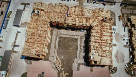 Multistory apartment complex under construction with timber wood frame, elevator vertical shaft, large courtyard, slab foundation, heavy equipment machines, downtown Dallas, Texas, aerial view. USA