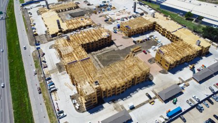 Apartment under construction near Interstate I-35E Stemmons Freeway downtown Dallas, timber wood frame, elevator vertical shaft, large courtyard, slab foundation, heavy equipment, aerial view. USA